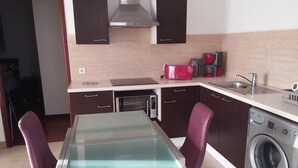 Cocina compacta con mesa de vidrio, lavadora y cafetera.