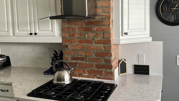 A kitchen with white cabinets, a brick chimney, a gas stove, and a wall clock. - The Whitehouse. (Green Cove Springs)