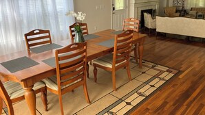 A dining area with a wooden table and chairs, a vase with flowers, and a patterned rug. - The Whitehouse. (Green Cove Springs)