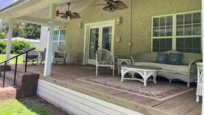 A covered porch with wicker furniture, ceiling fans, and a brick wall. - The Whitehouse. (Green Cove Springs)