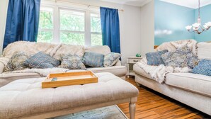 A living room with two sofas, a wooden coffee table, and a chandelier. - Tailgate House Near Stadium! Fire pit, basketball ct, pool table! Cozy and fun! (Manhattan)