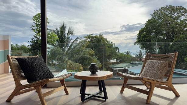 A balcony with two wicker chairs, a small round table, and a view of a tropical landscape. - Gorgeous 3 floor ocean front home. Private gated community. South Beach, Jaco!  (Jacó)