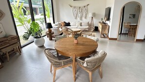 A spacious living room with a round wooden table and wicker chairs, a sofa, and a dining area with a mirror and plants. - Gorgeous 3 floor ocean front home. Private gated community. South Beach, Jaco!  (Jacó)