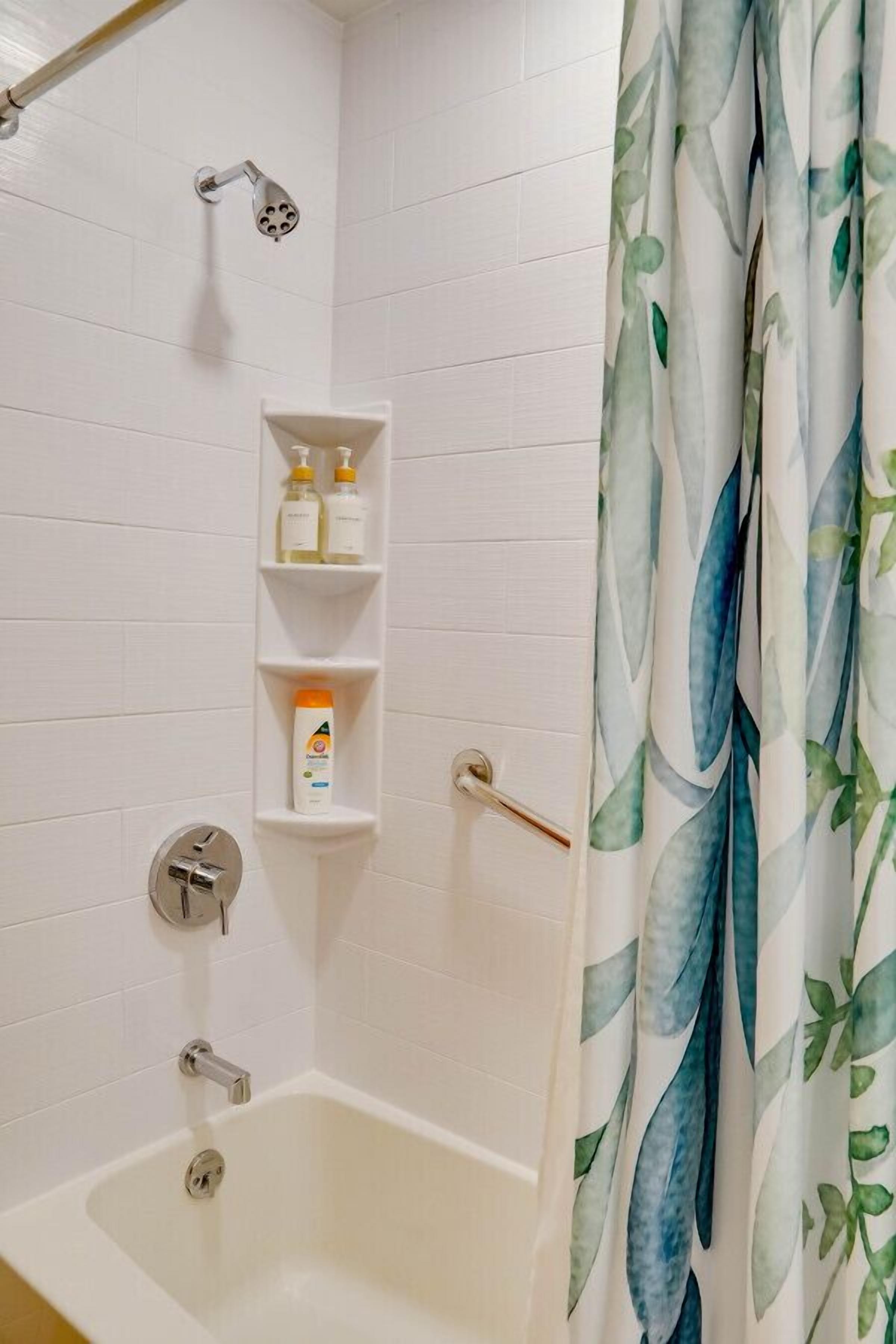 A bathroom with a bathtub, a showerhead, and a shelf with toiletries.