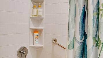 A bathroom with a bathtub, a showerhead, and a shelf with toiletries.