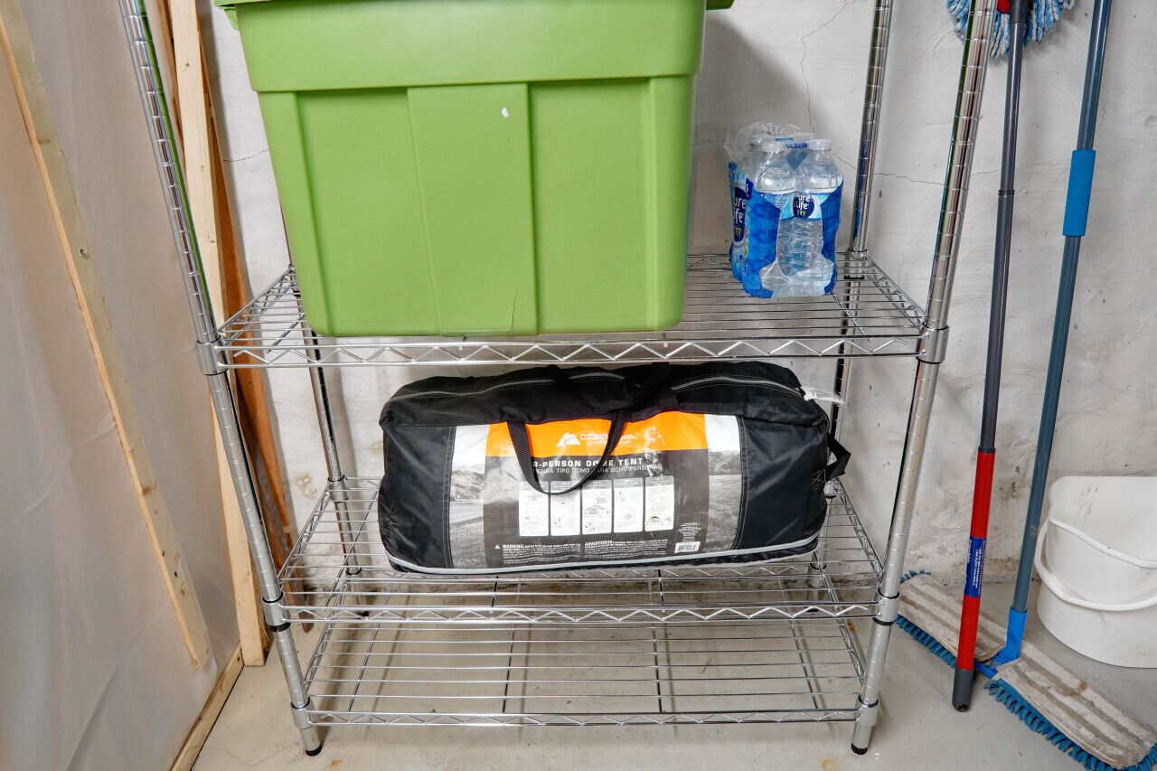 Une étagère métallique avec une boîte de rangement verte, un sac noir et deux bouteilles d’eau.