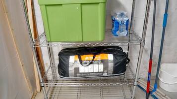 Une étagère métallique avec une boîte de rangement verte, un sac noir et deux bouteilles d’eau.