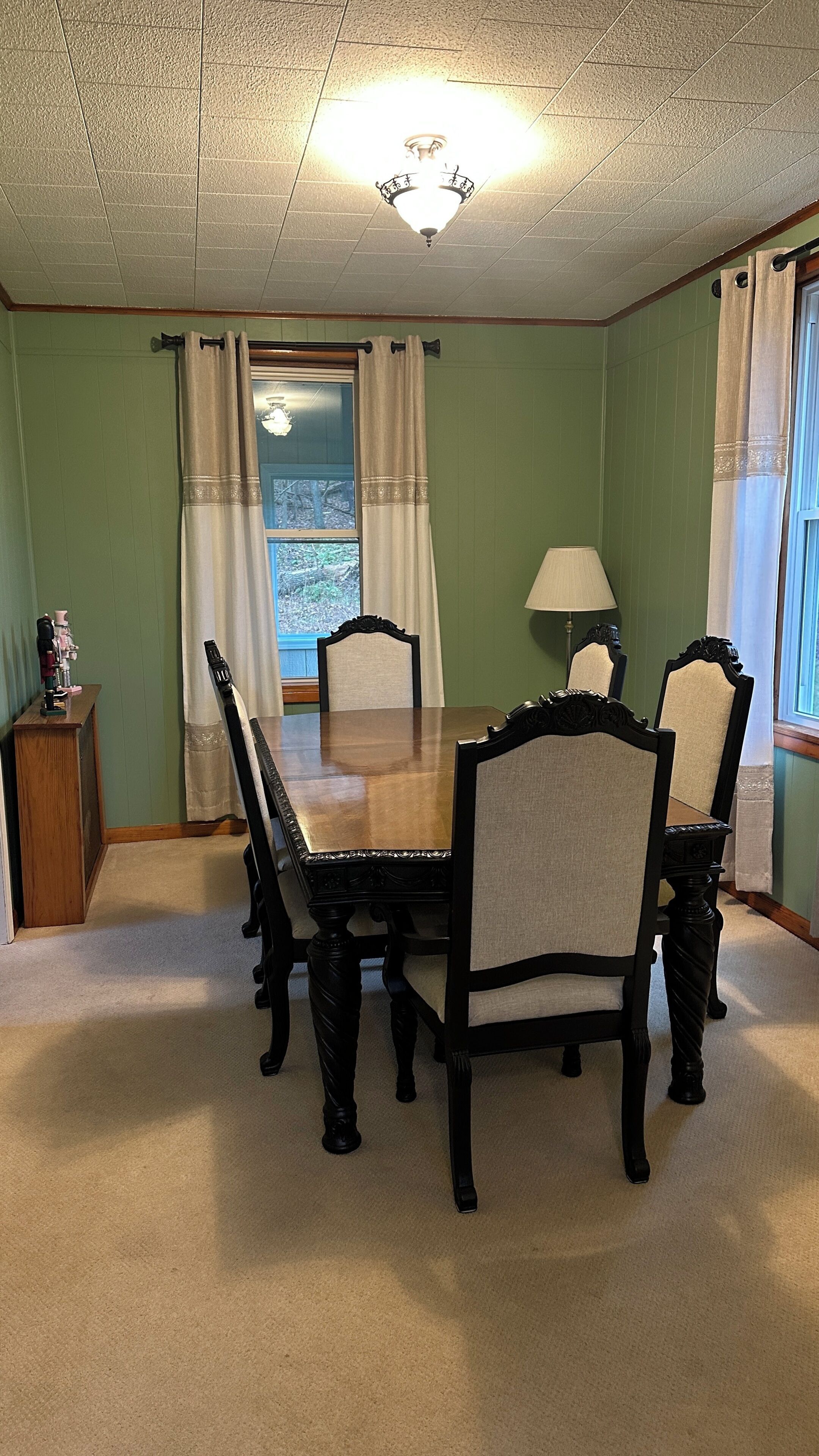 A dining room with a wooden table and chairs, a chandelier, and a window with curtains.