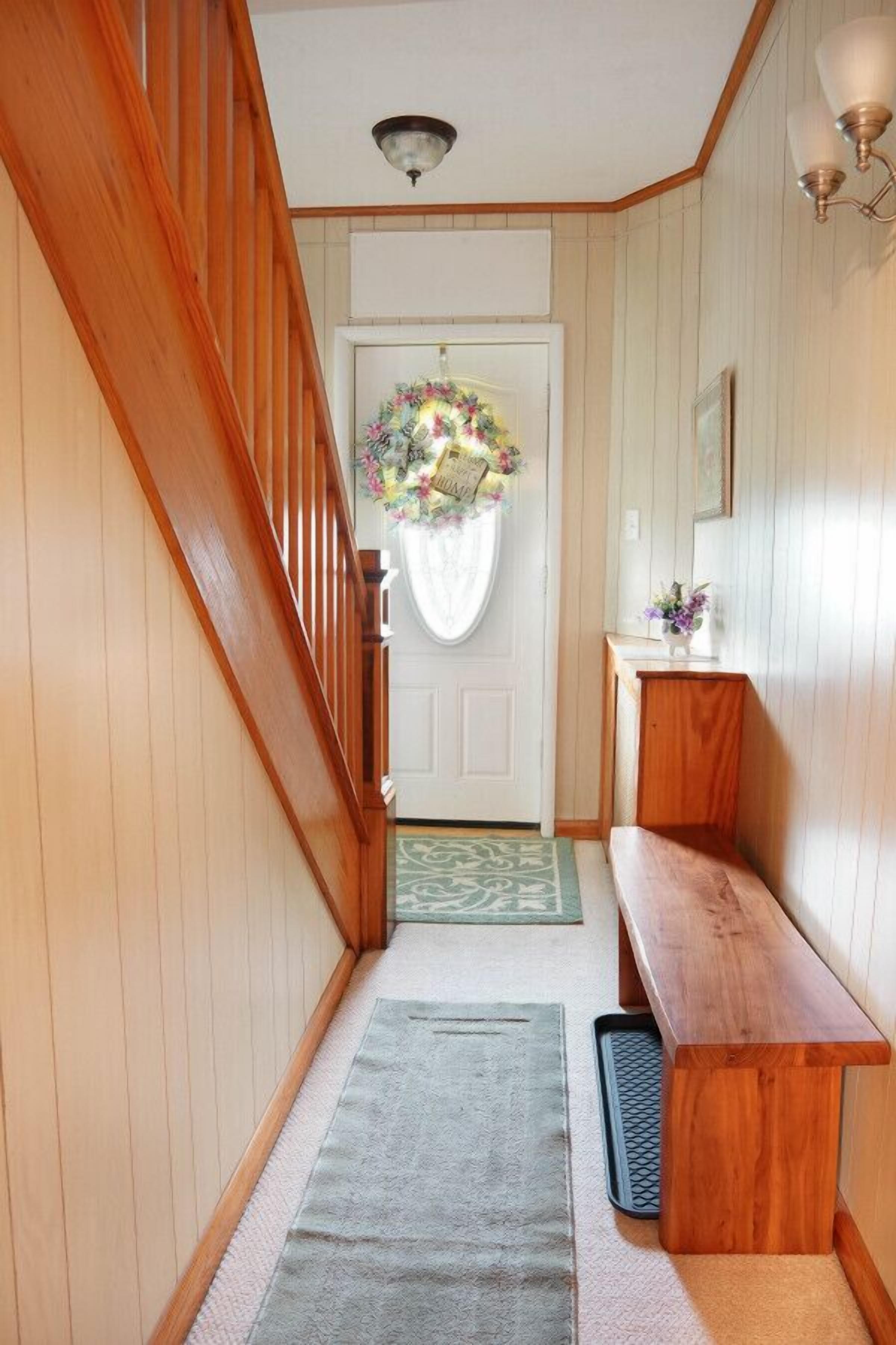 Un couloir aux murs en bois, un banc, une porte ornée d’une guirlande et un luminaire.
