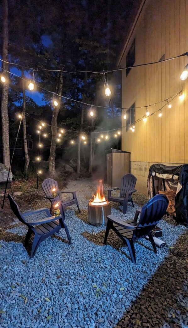 An outdoor seating area with four Adirondack chairs, a fire pit, and string lights. - Charming Retreat in the Hideout with a hot tub (Lake Ariel)
