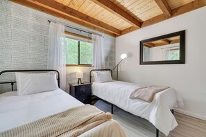 A bedroom with two beds, a nightstand, a mirror, and a window with curtains. - Charming Retreat in the Hideout with a hot tub (Lake Ariel)