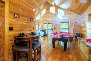 Un interior de madera con mesa de billar, una mesa de comedor con sillas y un lavabo rojo.