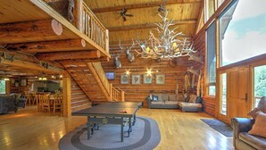 A spacious log cabin interior with a ping pong table, a chandelier, and a cozy seating area.
