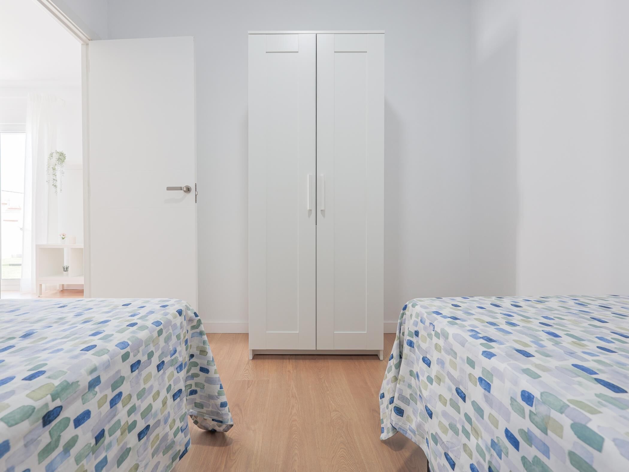 Une chambre avec deux lits, une armoire et une petite table sur laquelle est posée une plante.
