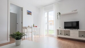 Una sala moderna con televisor de pantalla plana, un comedor con mesa y sillas, y un gran ventanal con cortinas.
