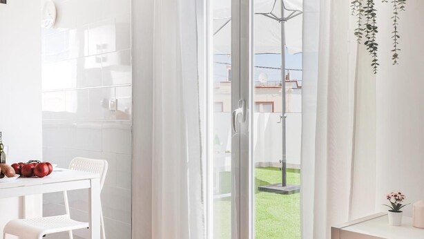 Una cocina luminosa y moderna con armarios blancos, una mesa de comedor con sillas y vistas a un césped verde a través de una puerta corrediza de vidrio.