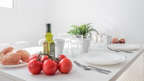 Ett rent, vitt matbord med en flaska olivolja, en krukväxt, en tallrik med tomater och en tallrik med småbröd.