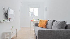 Ett modernt vardagsrum med en grå soffa, ett vitt TV-bord och ett litet bord med en växt.