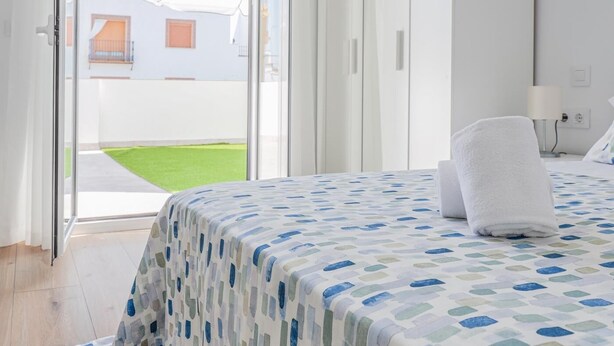 Ett hotellrum med en säng, en vit handduk och utsikt över en innergård med ett vitt parasoll.