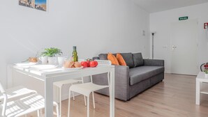 Ett modernt vardagsrum med en grå soffa, ett vitt soffbord och en matplats med ett vitt bord och stolar. Det står en liten växt på bordet och en inramad tavla hänger på väggen.