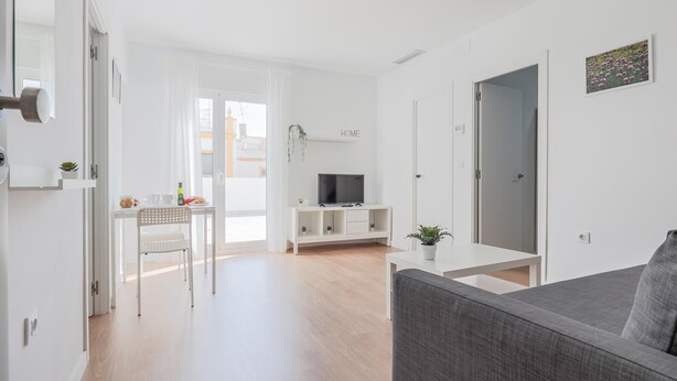 A modern living room with a grey sofa, a TV on a white stand, and a dining area with a table and chairs. - Apt high qualities 2 BR Algaba (La Algaba)