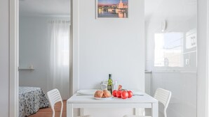 A modern, white-themed dining area with a table set for two, featuring bread, tomatoes, and a bottle. - Apt high qualities 2 BR Algaba (La Algaba)