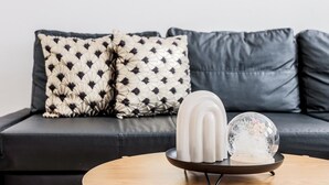 A modern living room with a dark leather sofa, patterned pillows, a white vase, and a glass sphere on a wooden coffee table.