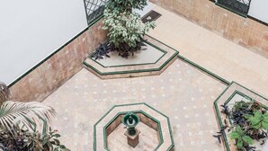 A courtyard with tiled flooring, a central fountain, and surrounding planters with various plants.