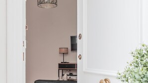 A doorway leading into a room with a dark leather ottoman, a lamp, and a television on a stand.