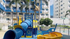 Un terrain de jeux avec un toboggan, des structures d’escalade et un petit véhicule jaune.