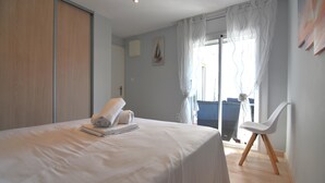 Un dormitorio con cama, una silla, un ventanal con cortinas y una puerta.
