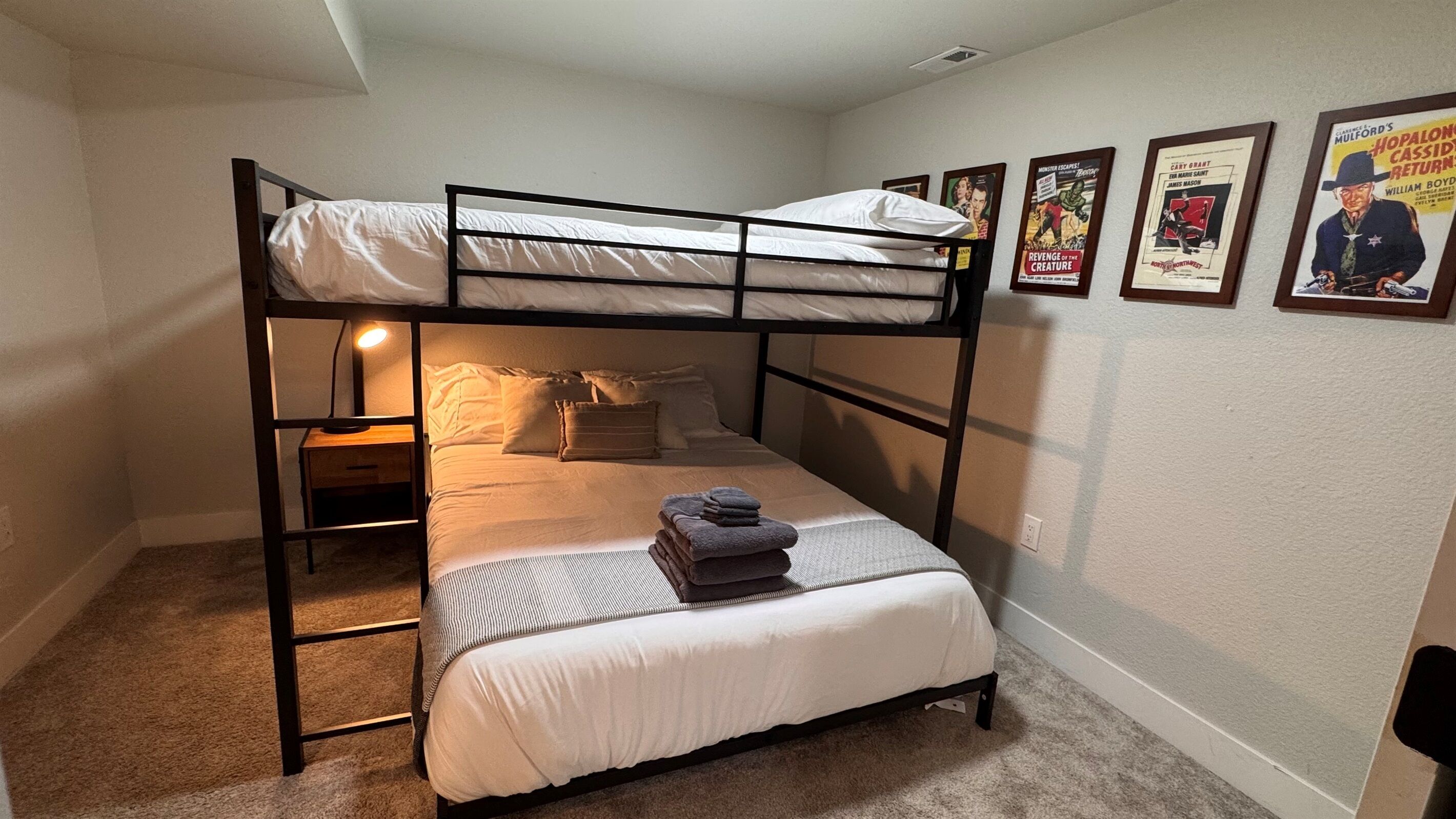Une chambre avec un lit superposé, un lit simple, une table de chevet, une lampe et des affiches accrochées au mur.