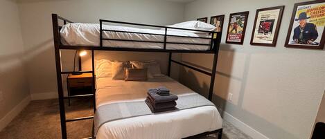 Une chambre avec un lit superposé, un lit simple, une table de chevet, une lampe et des affiches accrochées au mur.