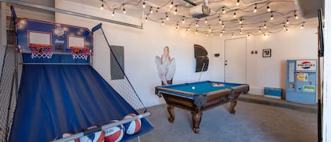 A recreational room with a basketball hoop, pool table, and string lights.