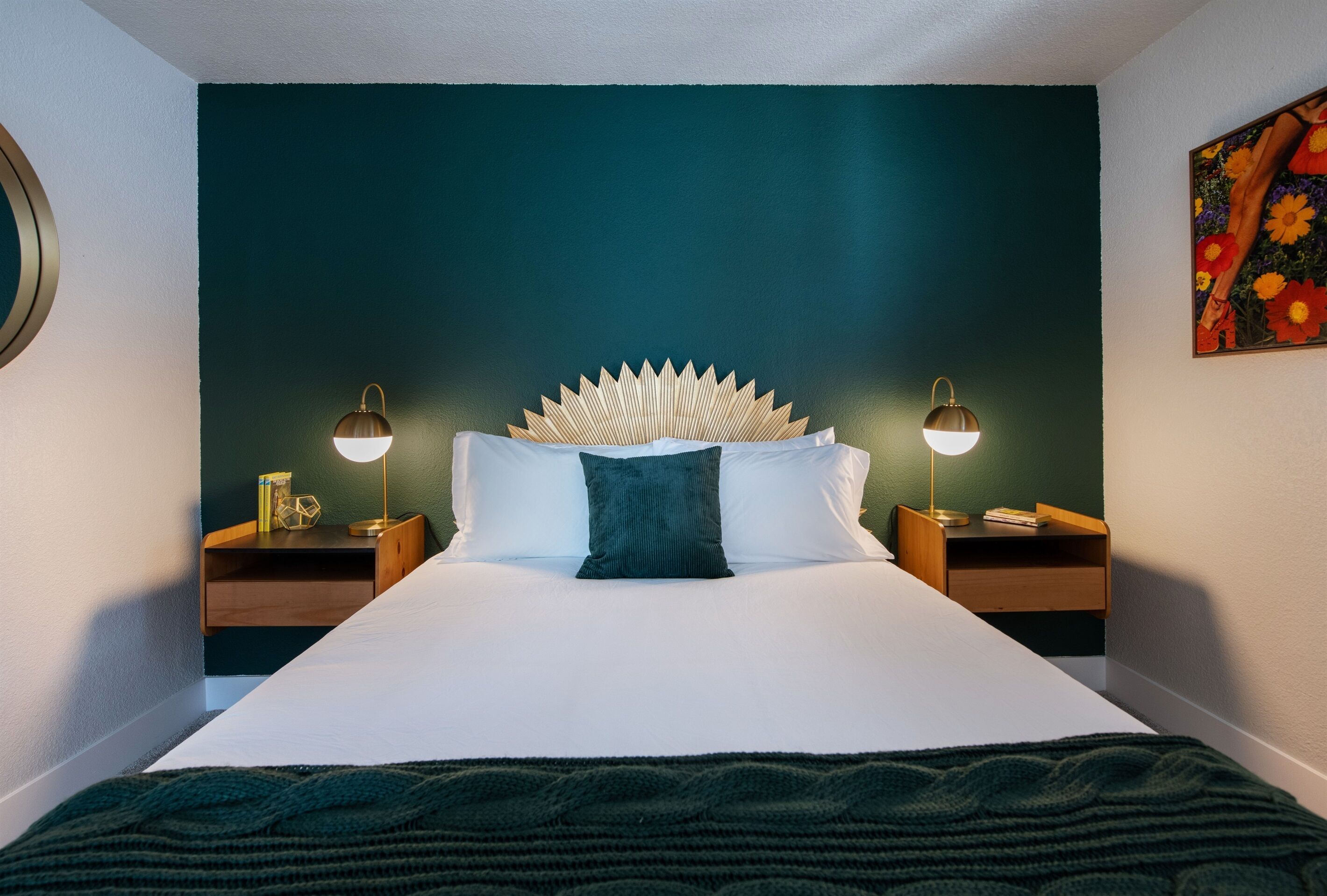 Un lit avec une tête de lit blanche, deux tables de chevet avec des lampes, un mur vert et un tableau.