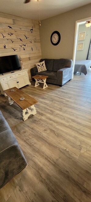 Ein Wohnzimmer mit Holzboden, einem grauen Sofa, einem weißen Schrank, einem Holztisch und einer Wanduhr.