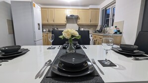 A modern kitchen with wooden cabinets, a built-in oven, and a dining area set with black plates, silverware, and a vase with white flowers. - Burnley Entire House 4-Bedrooms-Sleeps 6-Driveway (Burnley)