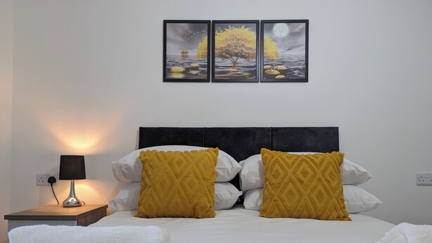 A neatly made bed with white and mustard pillows, a bedside lamp, and a blanket. - Burnley Entire House 4-Bedrooms-Sleeps 6-Driveway (Burnley)