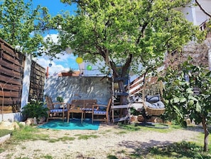 A patio with a wooden table and chairs, a hanging chair, and a small tree.