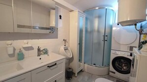 A bathroom with a sink, toilet, urinal, shower, and washing machine. - 2 Bedroom Apartment Sleeps 4 -Free Parking -Garden (Zadar)