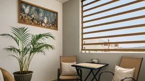 A cozy corner with a cushioned sofa, two chairs, a small table, a potted plant, a framed artwork, and a window with horizontal blinds. - Cabo Oasis Escape - 1 bedroom Apartment (Cabo San Lucas)