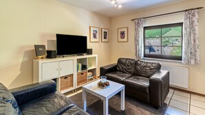 Een woonkamer met een bank, een salontafel, een televisie op een dressoir en een raam met gordijnen.