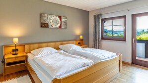 Een slaapkamer met een houten bed, twee nachtkastjes met lampen, een wandklok en een raam met uitzicht.