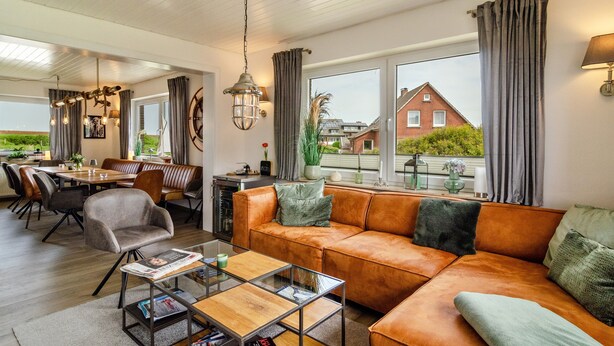 Ein modernes Wohnzimmer mit Ledersofa, Esstisch und Stühlen, großen Fenstern mit Vorhängen und Blick auf ein Haus.