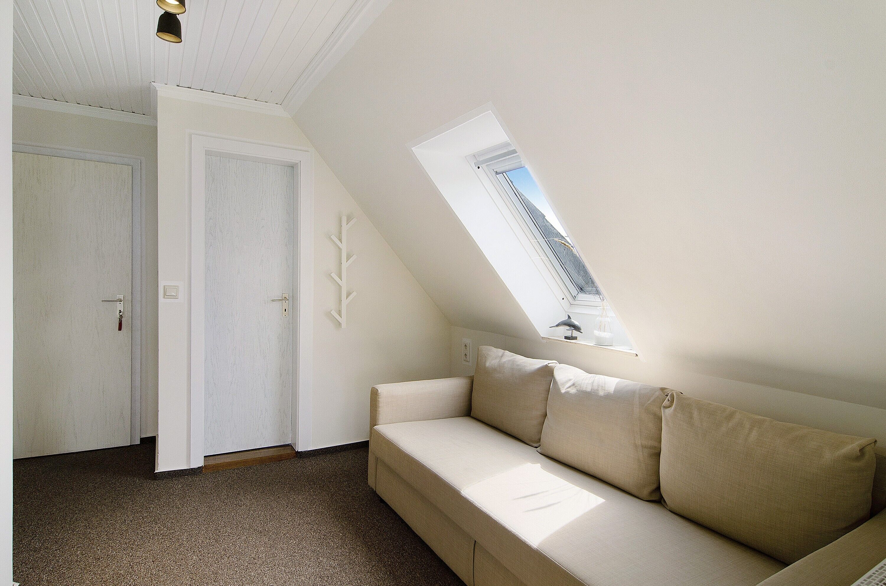 Een kamer met een schuine kap, een raam, een bank en een deur.