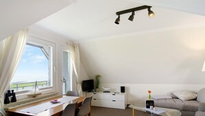 Ein modernes Zimmer mit Essbereich, einer Couch, einem Fernseher und einem Fenster mit Vorhängen.