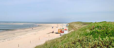Een strand met een uitkijktoren, zandstrand en duinen met gras.