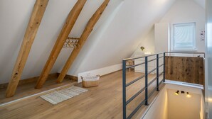 A loft bedroom with exposed wooden beams, a wooden floor, a metal railing, and a small window with blinds. - Apartment "Annele" with Private Terrace & Wi-Fi (Loßburg)
