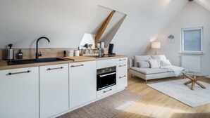 A modern kitchen with a built-in oven, a sink, and a wooden countertop. There is a white sofa and a glass coffee table in the living area. - Apartment "Annele" with Private Terrace & Wi-Fi (Loßburg)