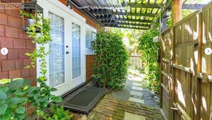 A covered patio area with a wooden pergola, a wooden fence, and a small garden with plants and a stepping stone path. - Centrally located private studio in Chemainus (Chemainus)